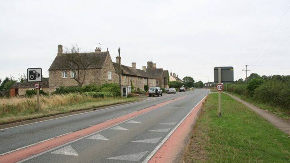 A rural road with houses, a speed limit sign, and a pedestrian crossing.