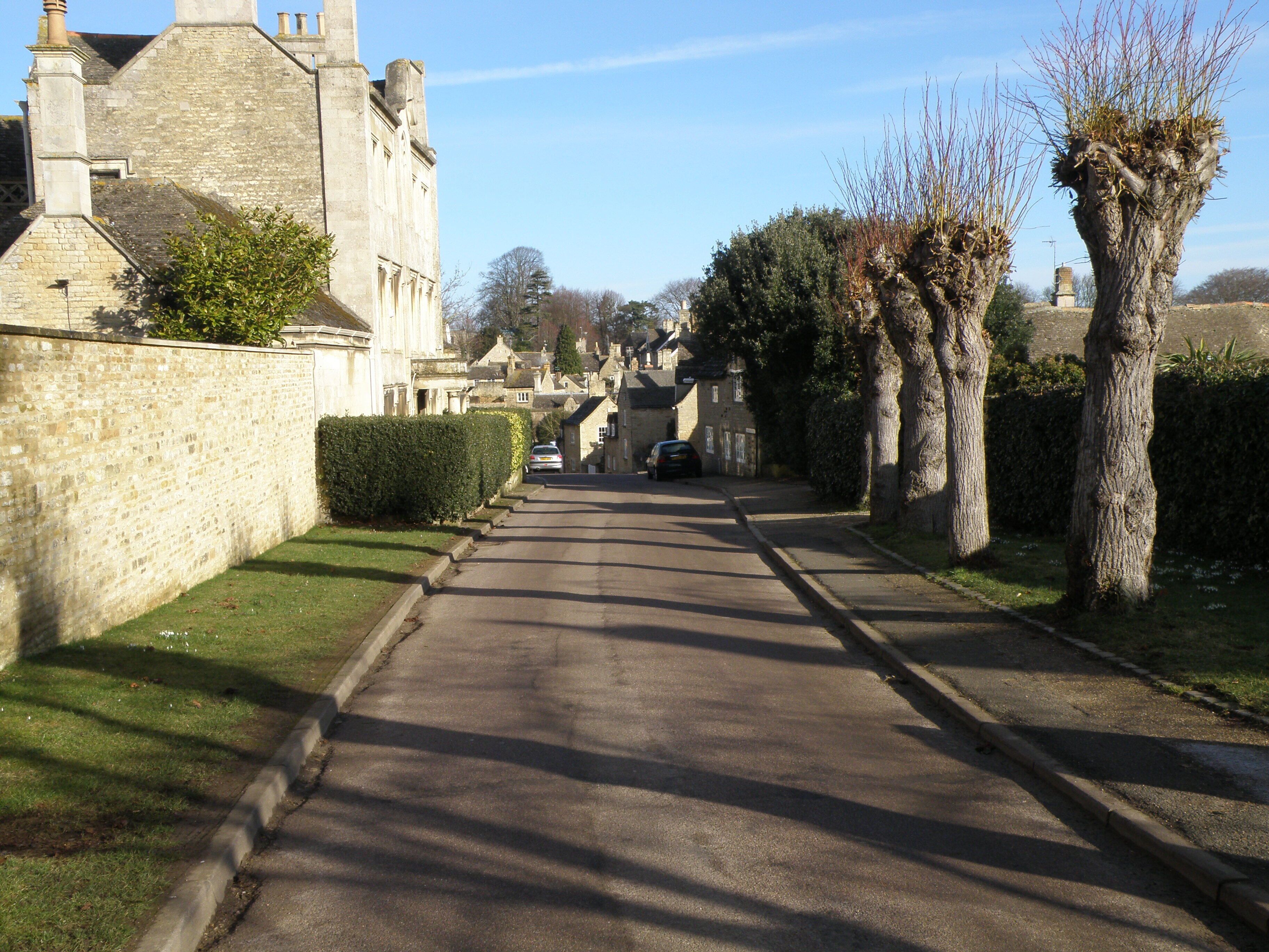 A narrow street flanked by stone buildings and trees.