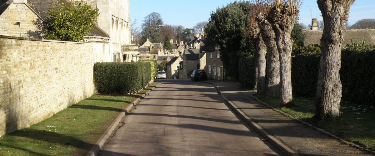 A narrow street flanked by stone buildings and trees.