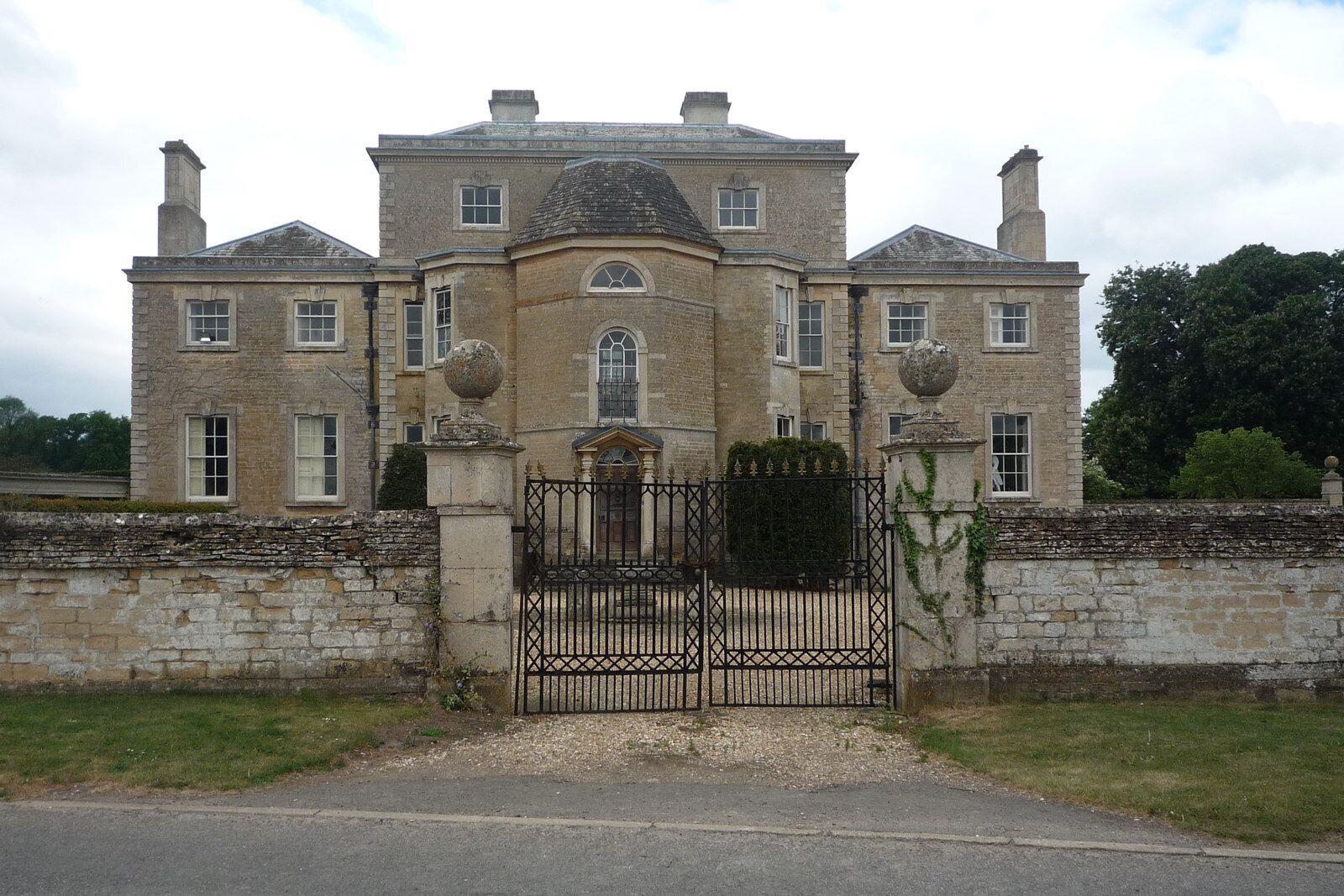 A large, historic stone building with a symmetrical facade, a central dome, and a gated entrance.