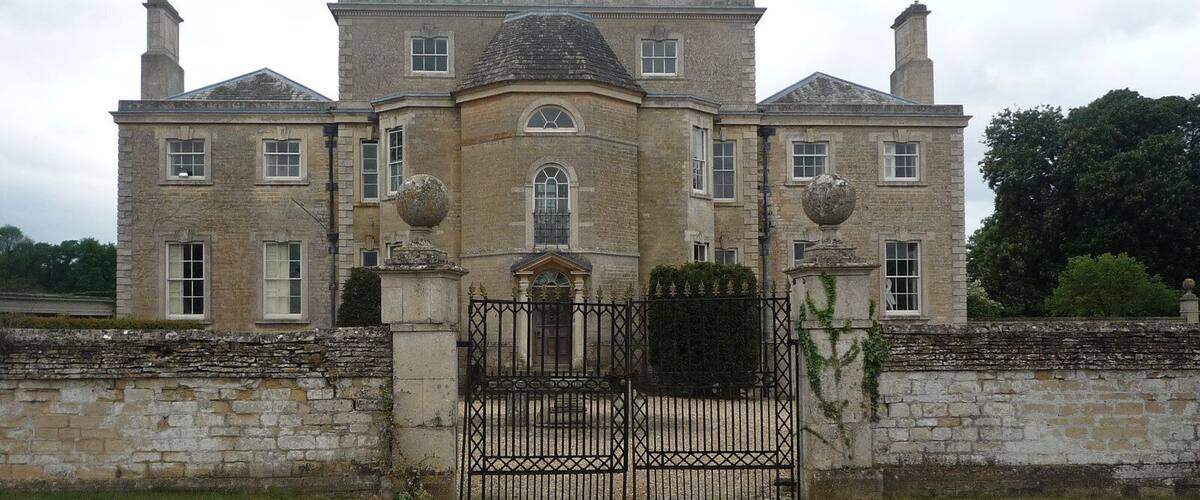 A large, historic stone building with a symmetrical facade, a central dome, and a gated entrance.