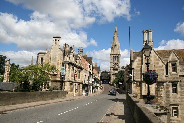 A historic street with stone buildings, a church spire, and a lamppost.