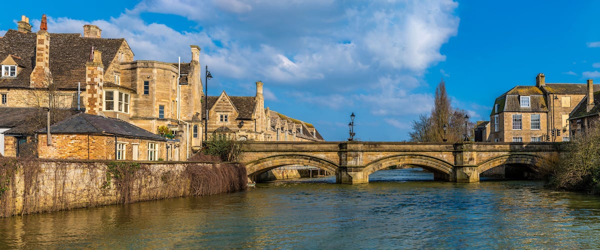 A stone bridge over a river with historic buildings on either side.