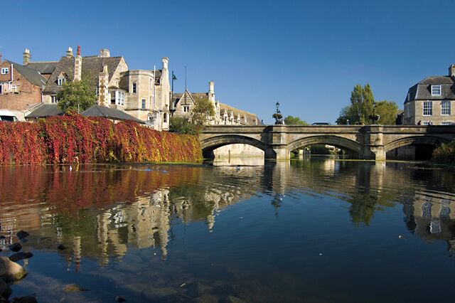 A stone bridge over a calm river, reflecting buildings and trees.