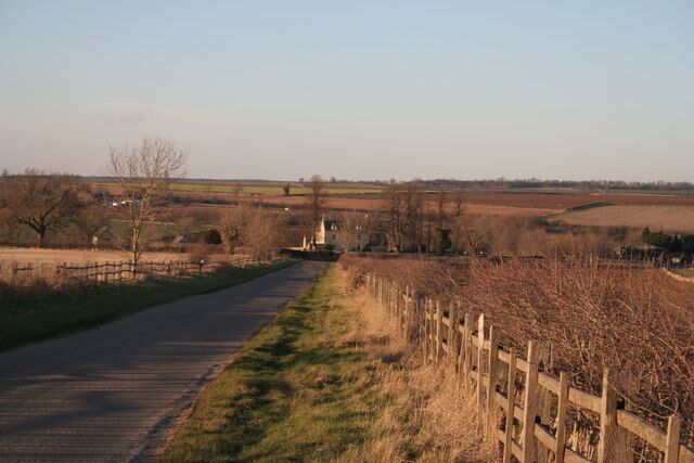 A rural road with a wooden fence on one side and fields on the other.