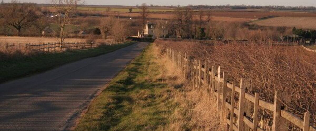 A rural road with a wooden fence on one side and fields on the other.