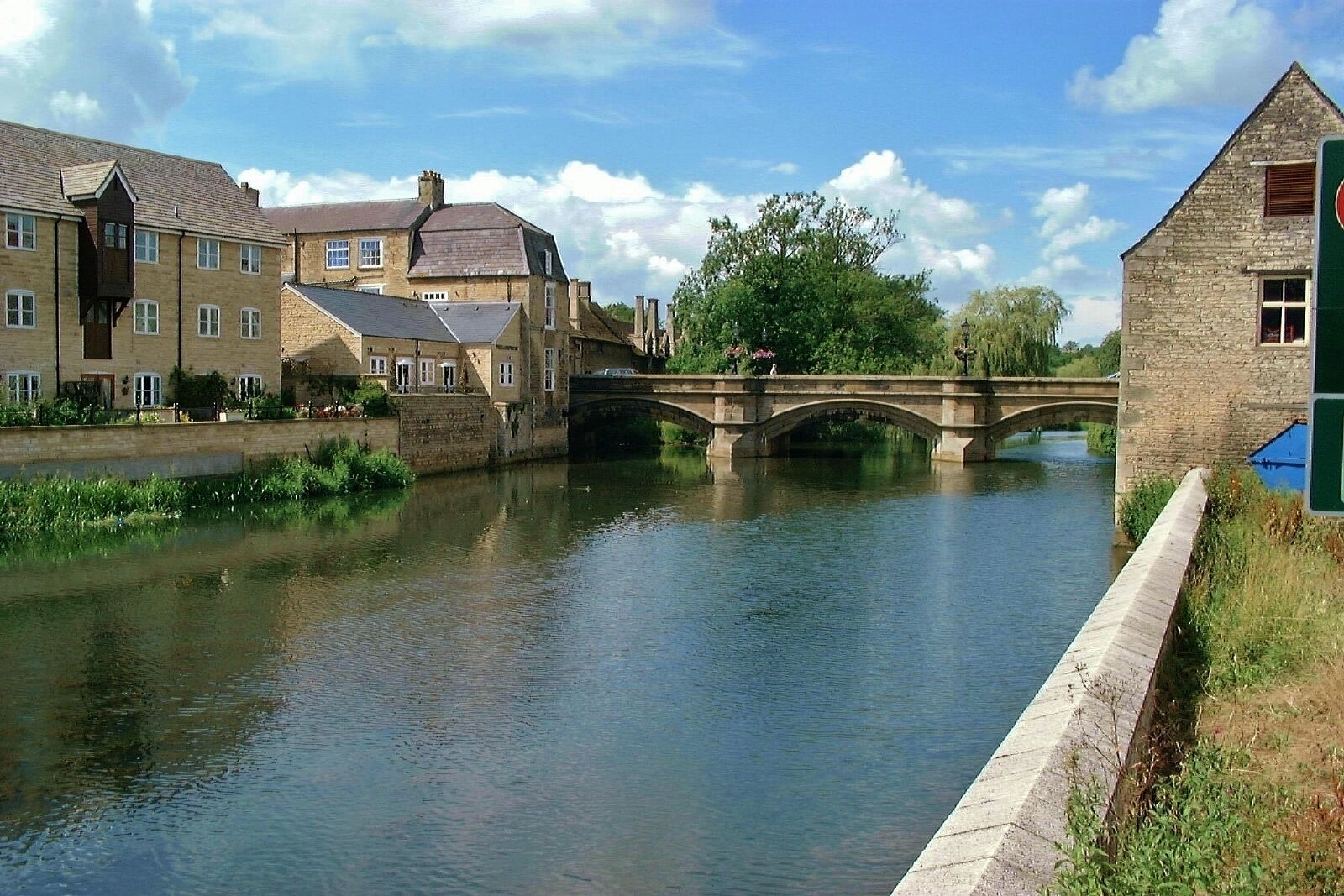 A stone bridge over a calm river, surrounded by historic buildings and lush greenery.