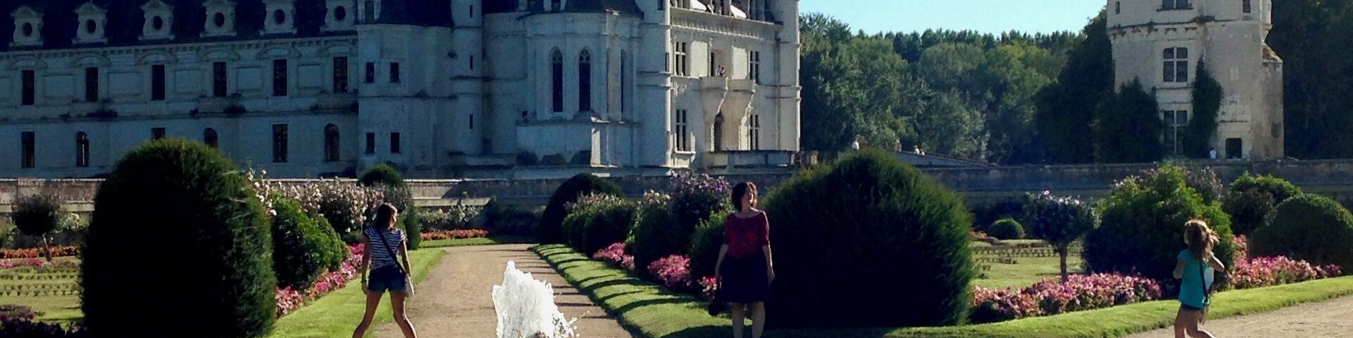 Un edificio histórico grande con múltiples torres y un jardín bien cuidado con una fuente.