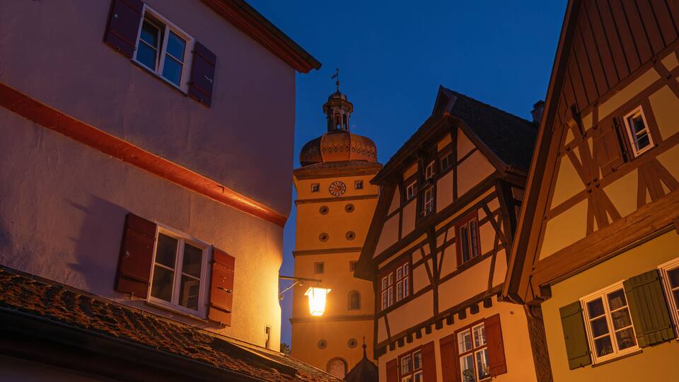 A traditional European town with half-timbered houses and a prominent tower with a clock.