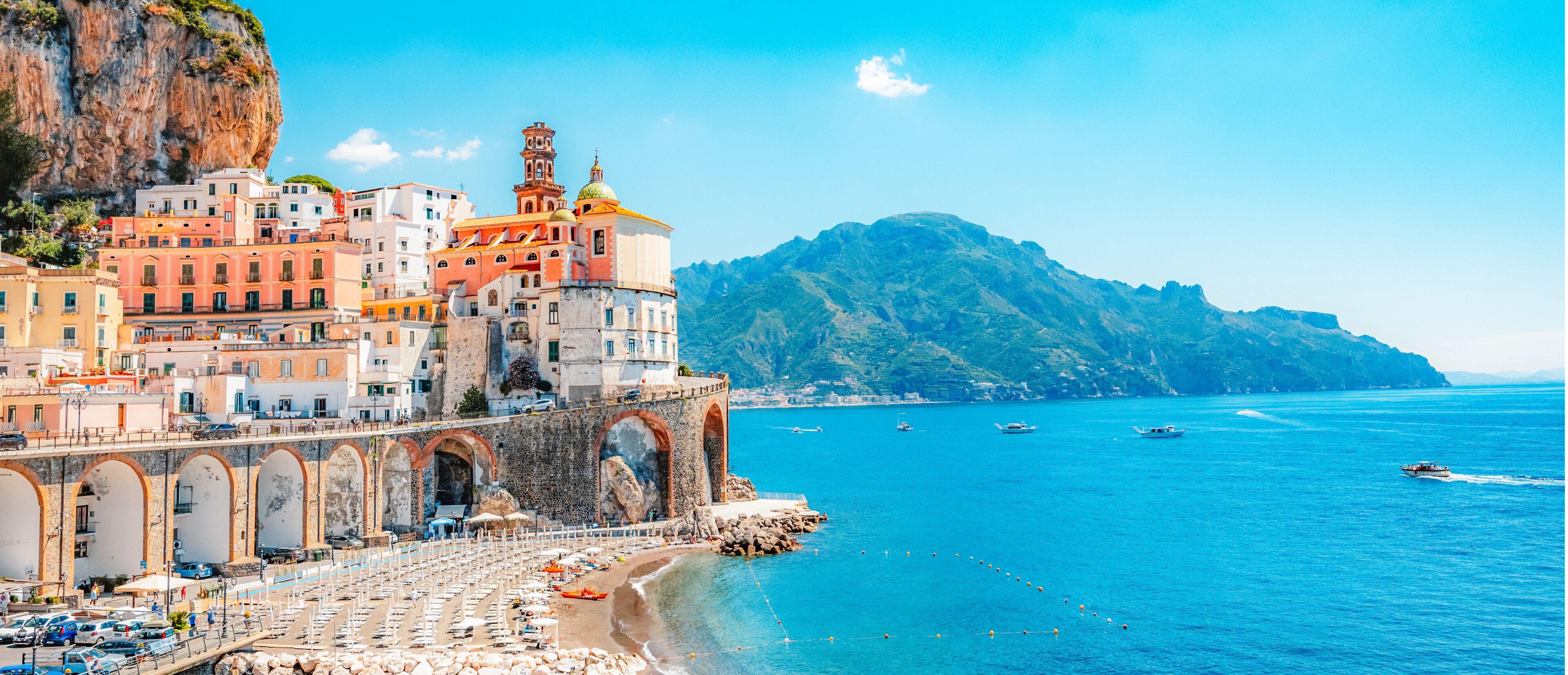 A coastal town with historic buildings, a prominent church with a bell tower, and a mountainous backdrop.
