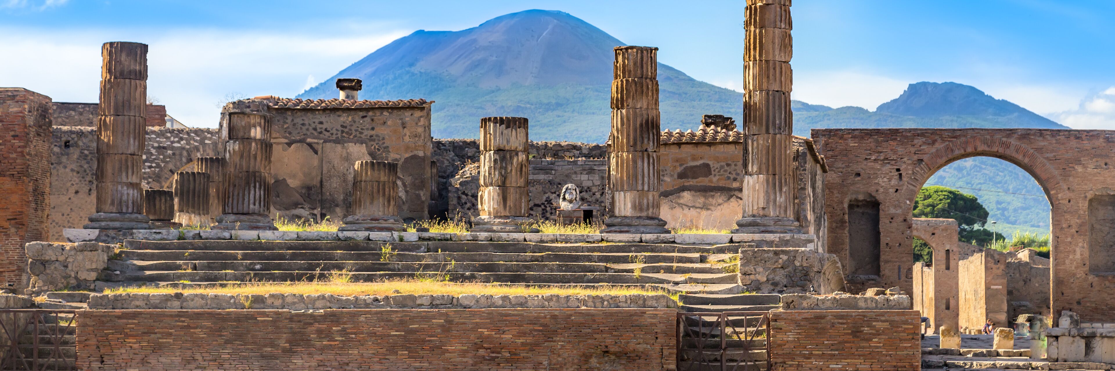 Ancient ruins with columns and an archway, set against a mountainous backdrop.