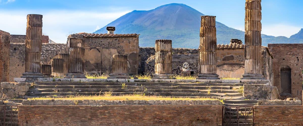Ancient ruins with columns and an archway, set against a mountainous backdrop.