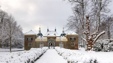 Um edifício coberto de neve com uma cúpula central e duas torres, cercado por árvores e arbustos carregados de neve.