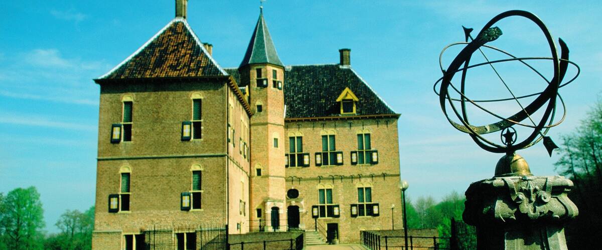 A large, historic building with a prominent tower and a sundial in the foreground.