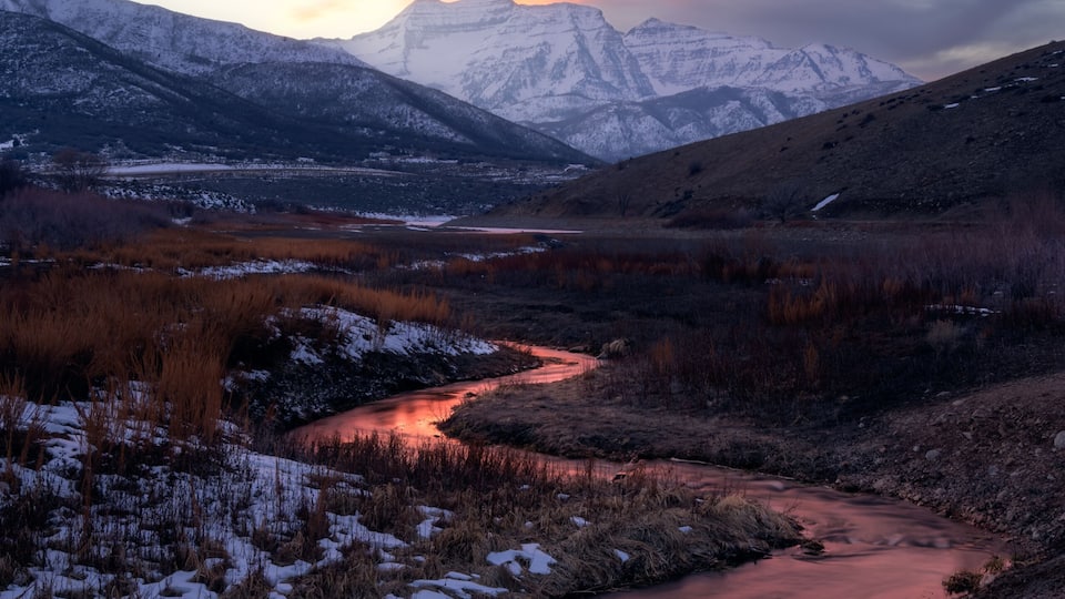 A river flowing through a snowy landscape with mountains in the background.