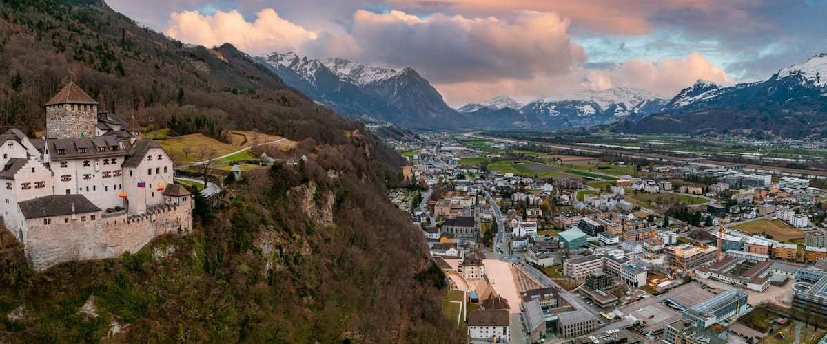Een kasteel op een heuvel met uitzicht op een stad, met bergen op de achtergrond.