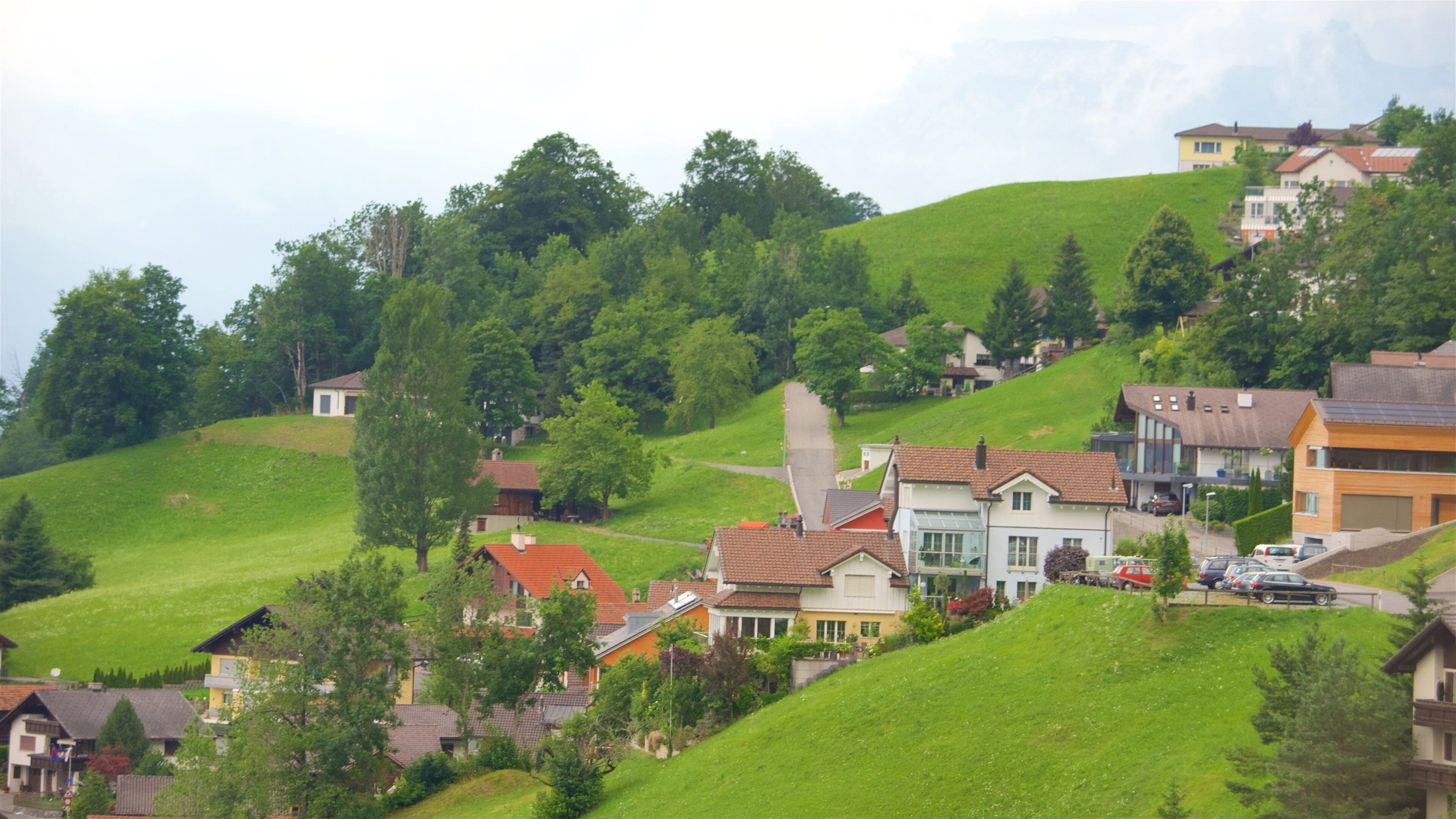 A hillside village with houses, green fields, and trees.
