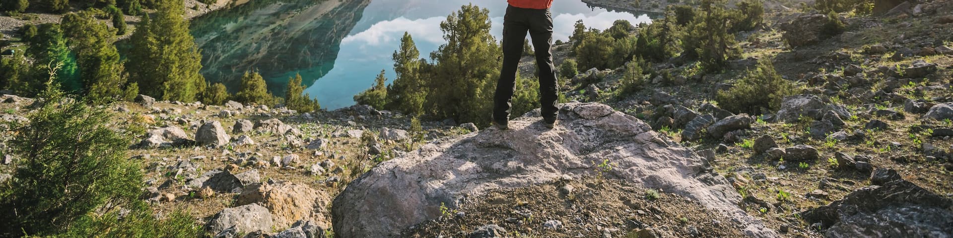hiker in red jacket raise his hands at a beautiful mountain lake at sunrise