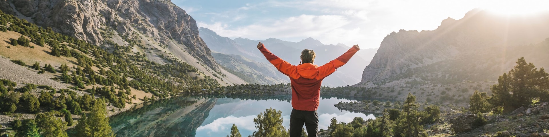 hiker in red jacket raise his hands at a beautiful mountain lake at sunrise