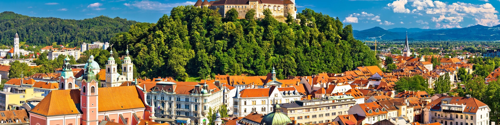 Eine historische Burg auf einem Hügel, umgeben von einer dicht bebauten Stadt mit traditioneller Architektur und blauem Himmel.