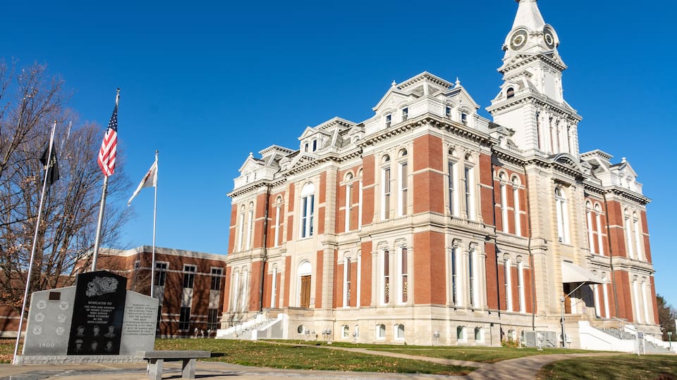 A large, historic building with a prominent clock tower and a flagpole with the American flag.