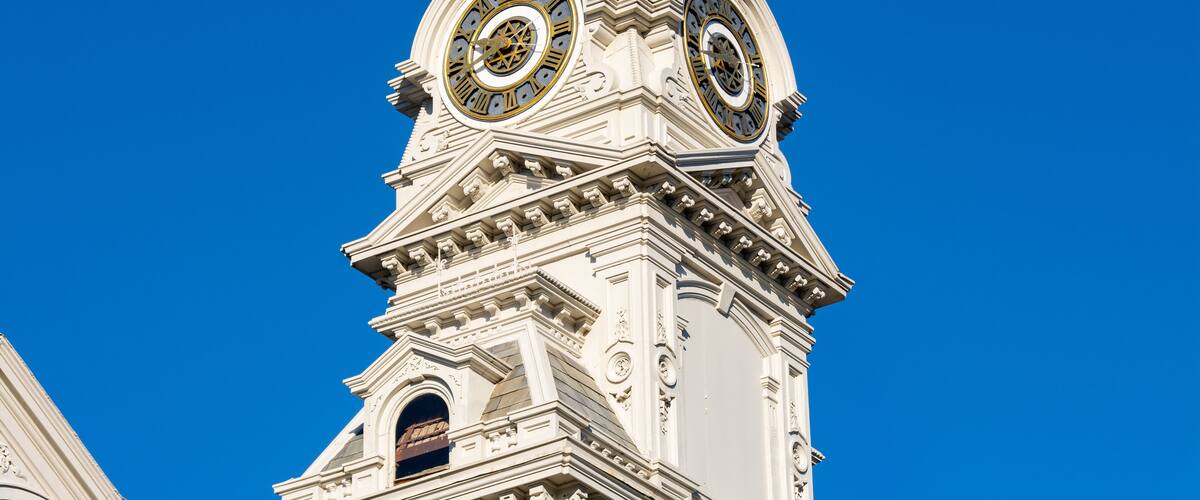 Een witte toren met twee grote klokken en gedetailleerde architectuur tegen een heldere blauwe lucht.