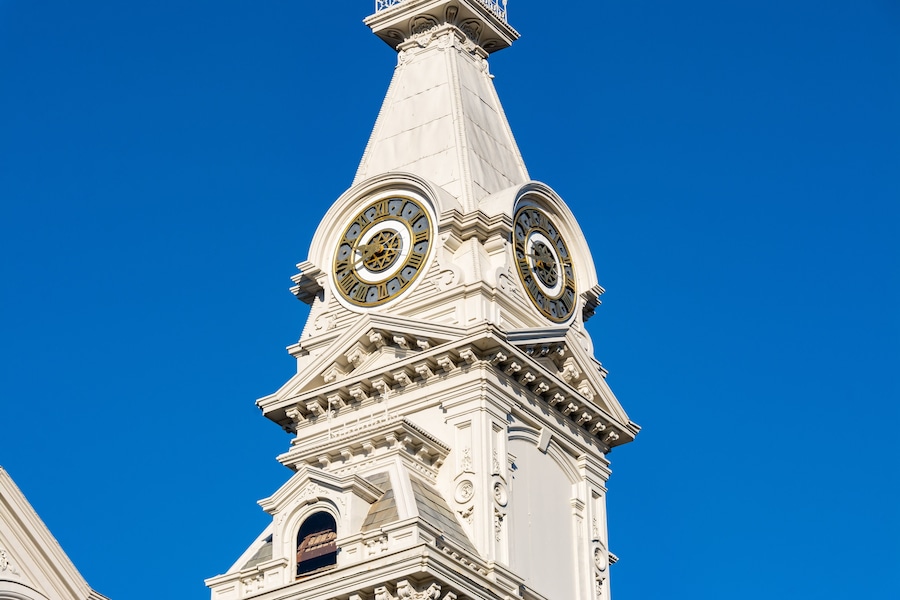 Een witte toren met twee grote klokken en gedetailleerde architectuur tegen een heldere blauwe lucht.