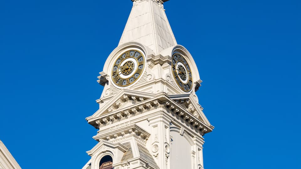 A white tower with two large clocks and intricate architectural details against a clear blue sky.