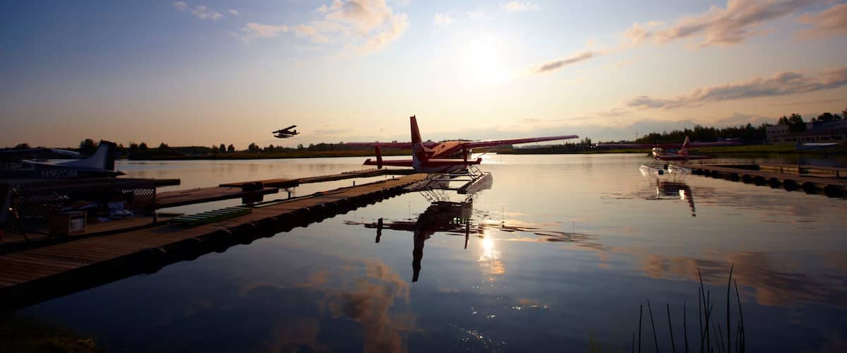A seaplane docked at a calm lake with a sunset in the background.