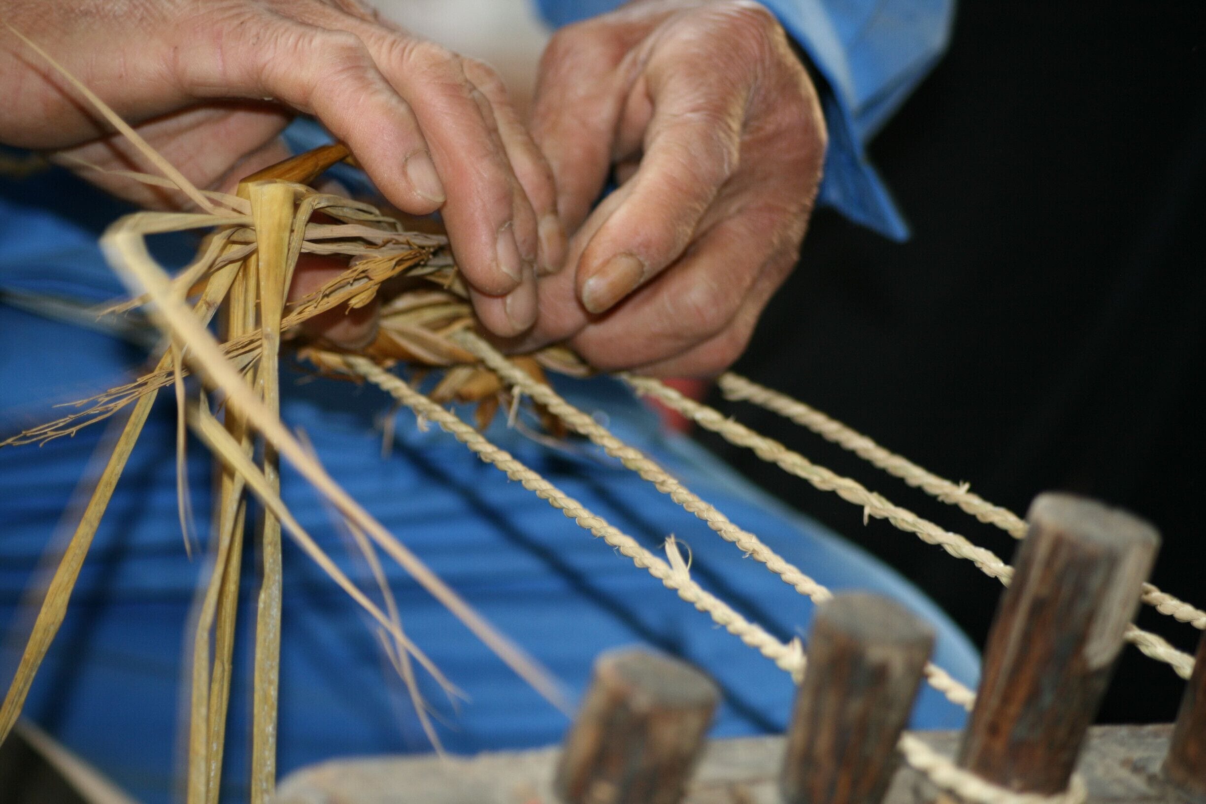 Hands weaving straw into a rope.
