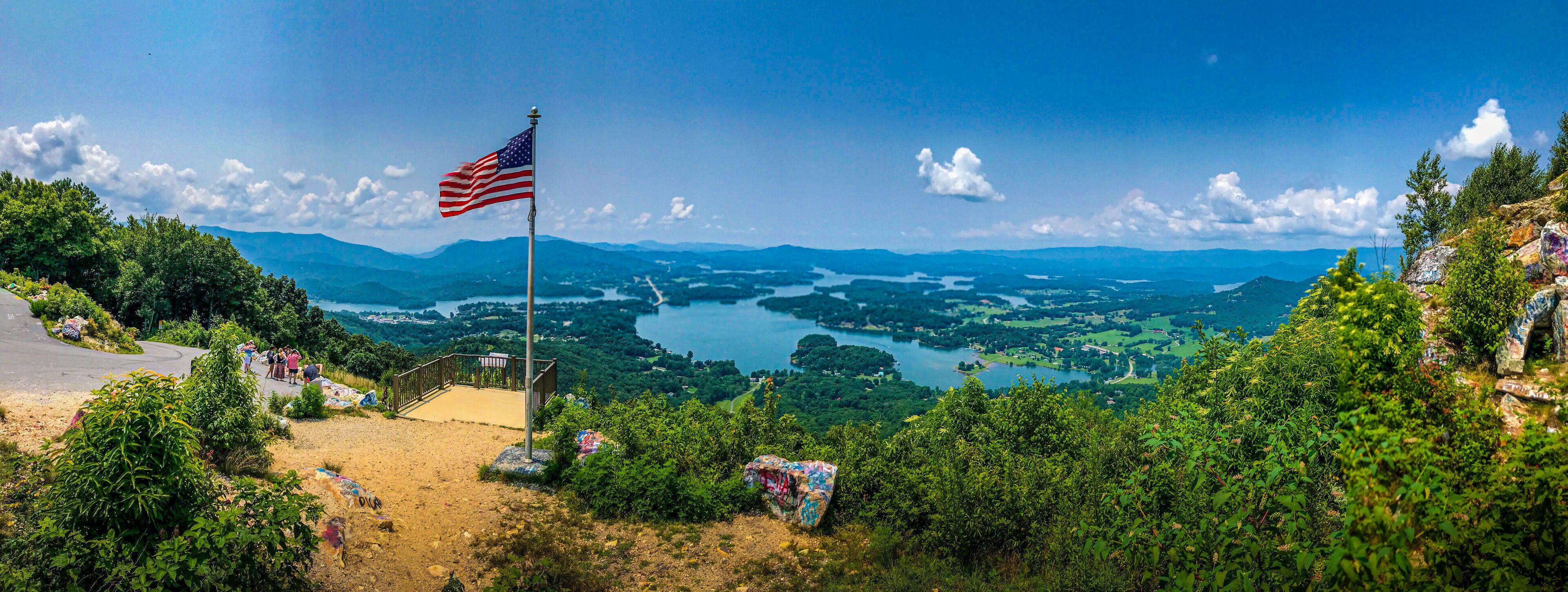 A flag on a hill overlooking a lake surrounded by mountains.