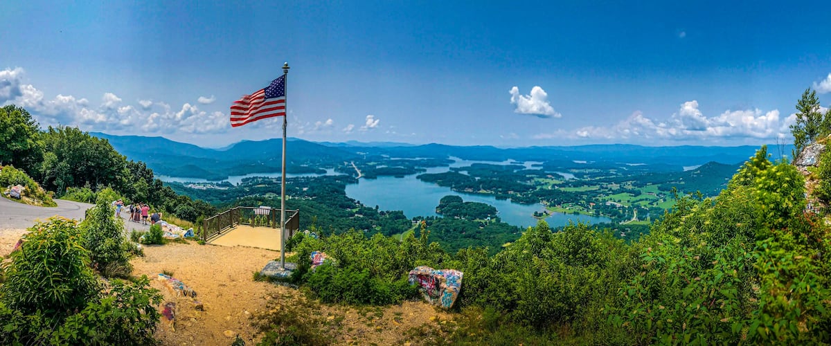 A flag on a hill overlooking a lake surrounded by mountains.