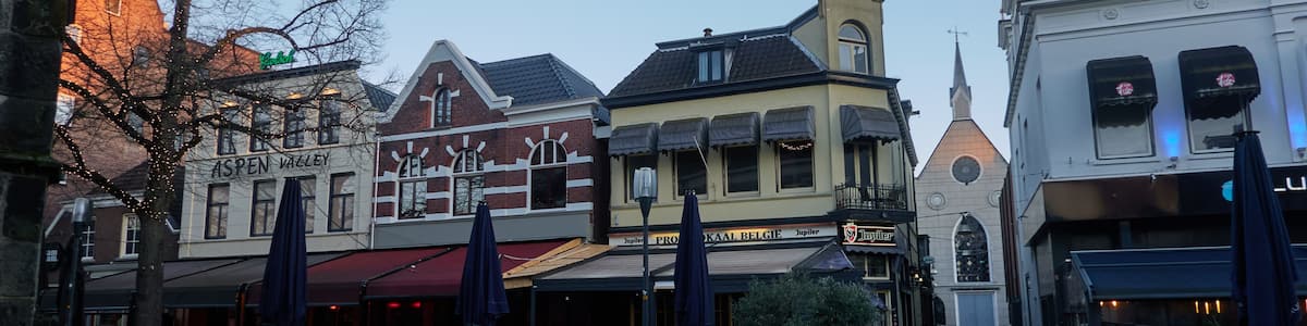 A cobblestone street lined with historic buildings, outdoor seating, and a church steeple.
