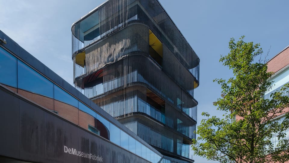 A modern building with a curved facade and a sign reading 'DeMuseumFabrik.'