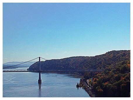 A suspension bridge over a river with hills in the background.