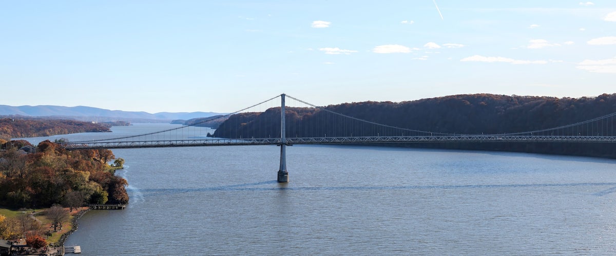 A suspension bridge over a river with autumn foliage and distant hills.