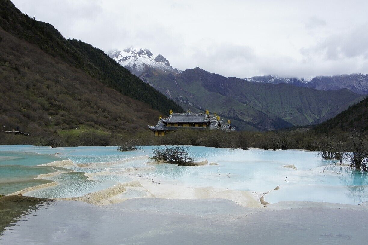 A traditional building surrounded by a mountainous landscape with a turquoise lake.