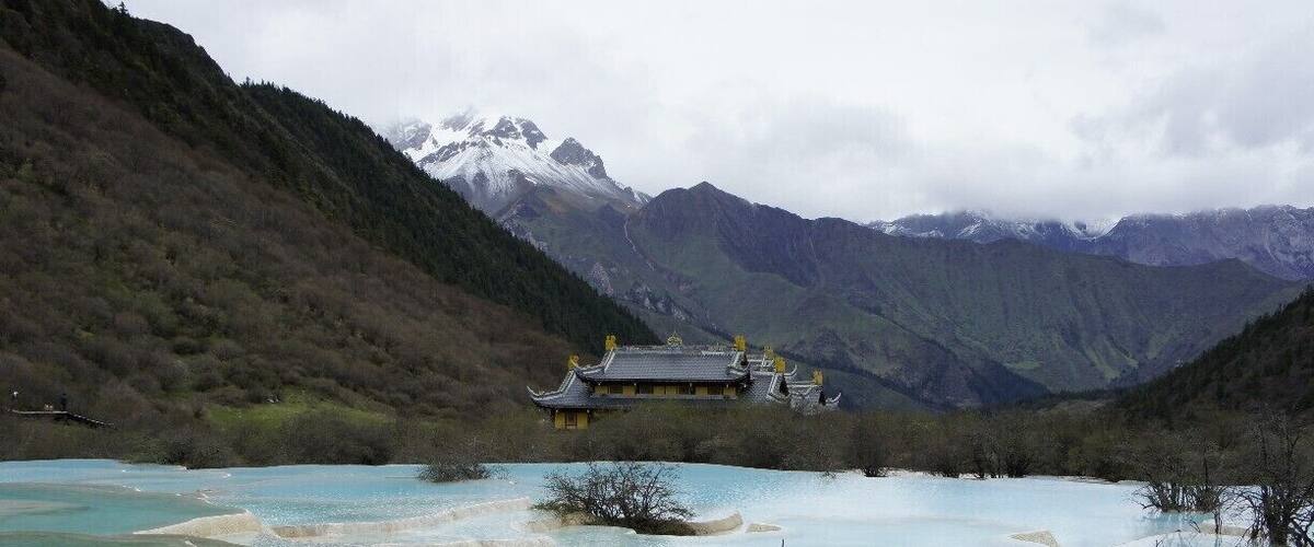 A traditional building surrounded by a mountainous landscape with a turquoise lake.