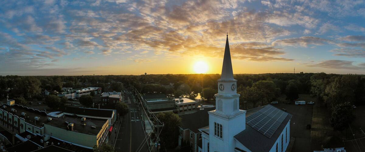 A church with a steeple and clock tower, surrounded by trees and buildings.