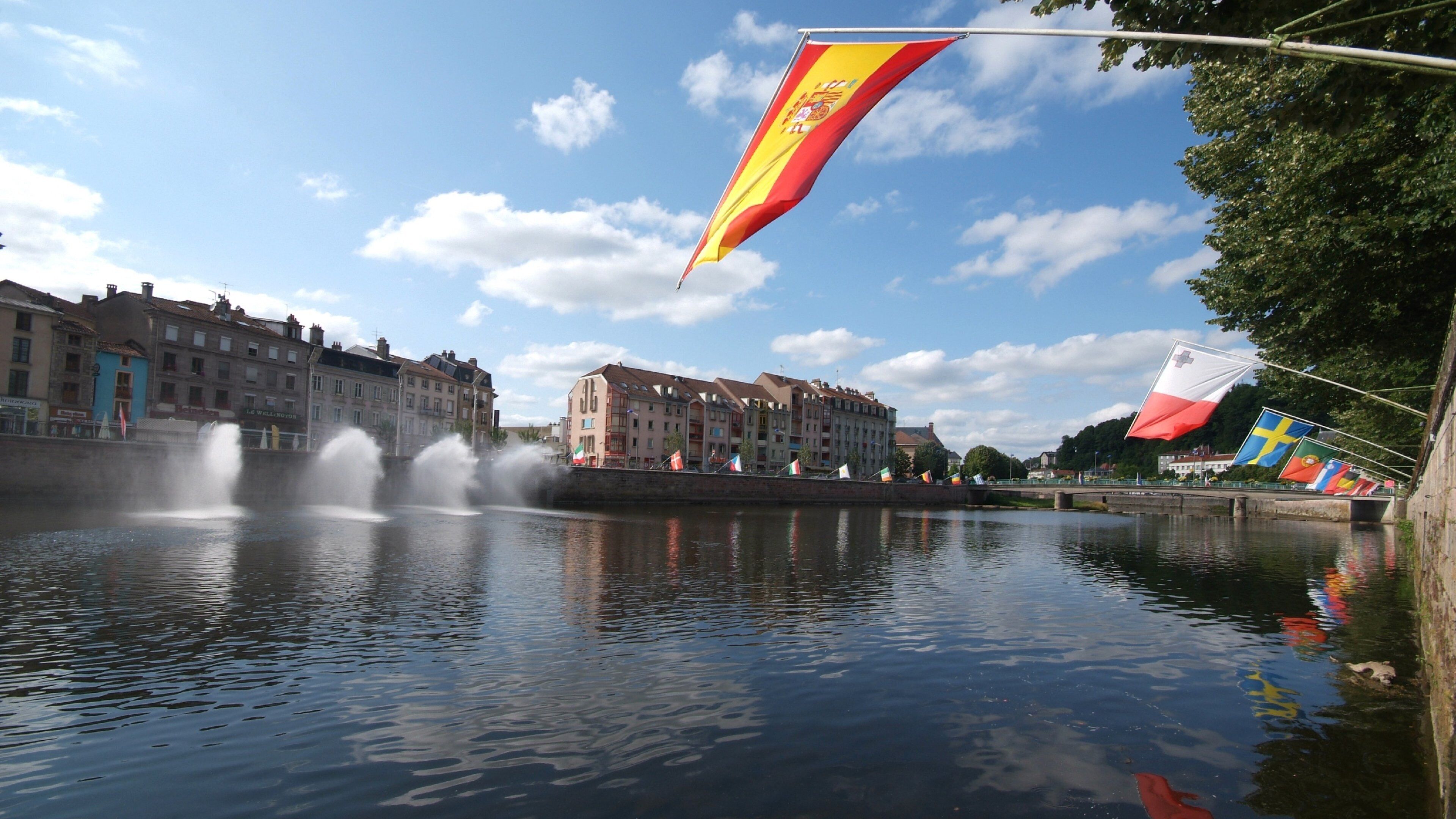 A river with fountains, buildings, and flags.