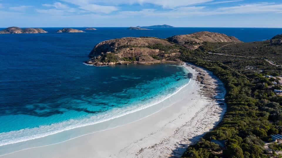 A coastal landscape with a sandy beach, clear turquoise waters, and rocky hills.