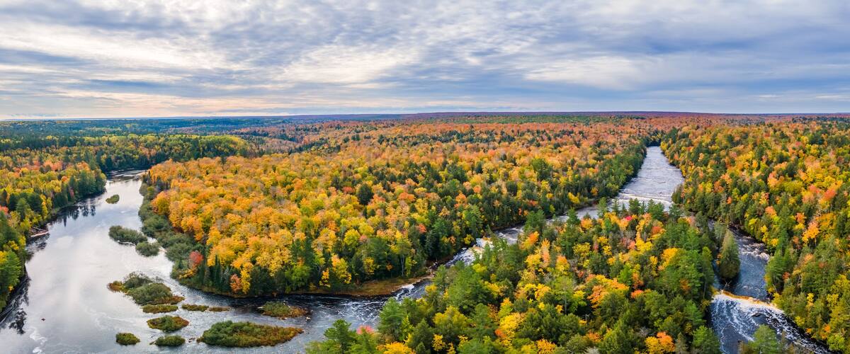 A river winding through a dense forest with autumn foliage.