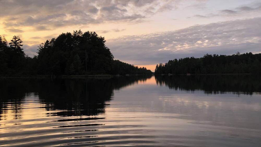Un lac paisible au coucher du soleil, avec des arbres qui se reflètent dans le ciel.