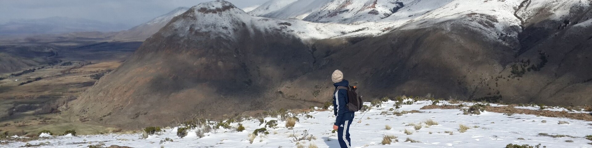 Una persona de pie sobre una montaña nevada, con vistas a picos nevados al fondo.