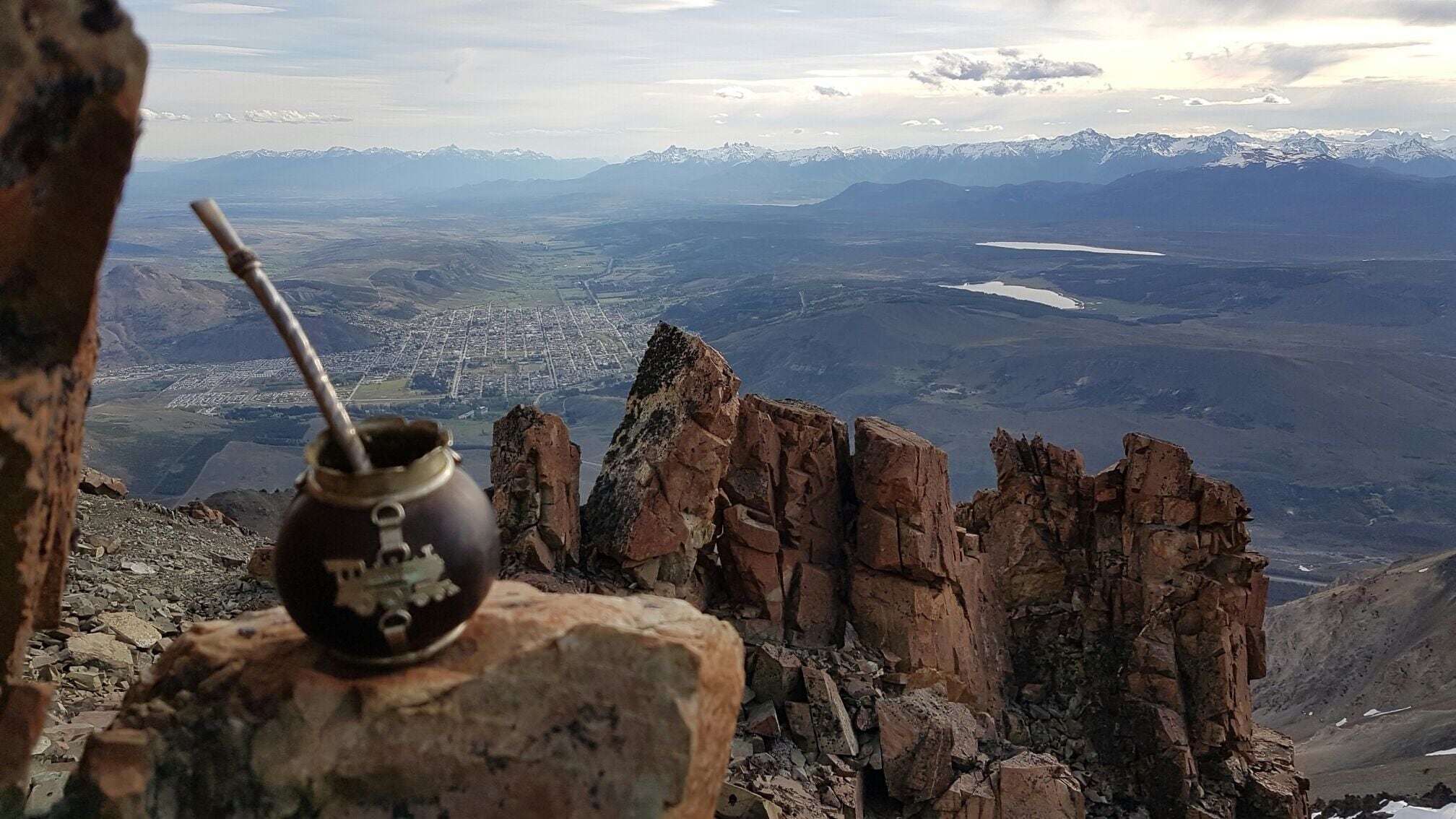 A view of a mountainous landscape with a clear sky, a distant city, and a traditional drink vessel on a rock.