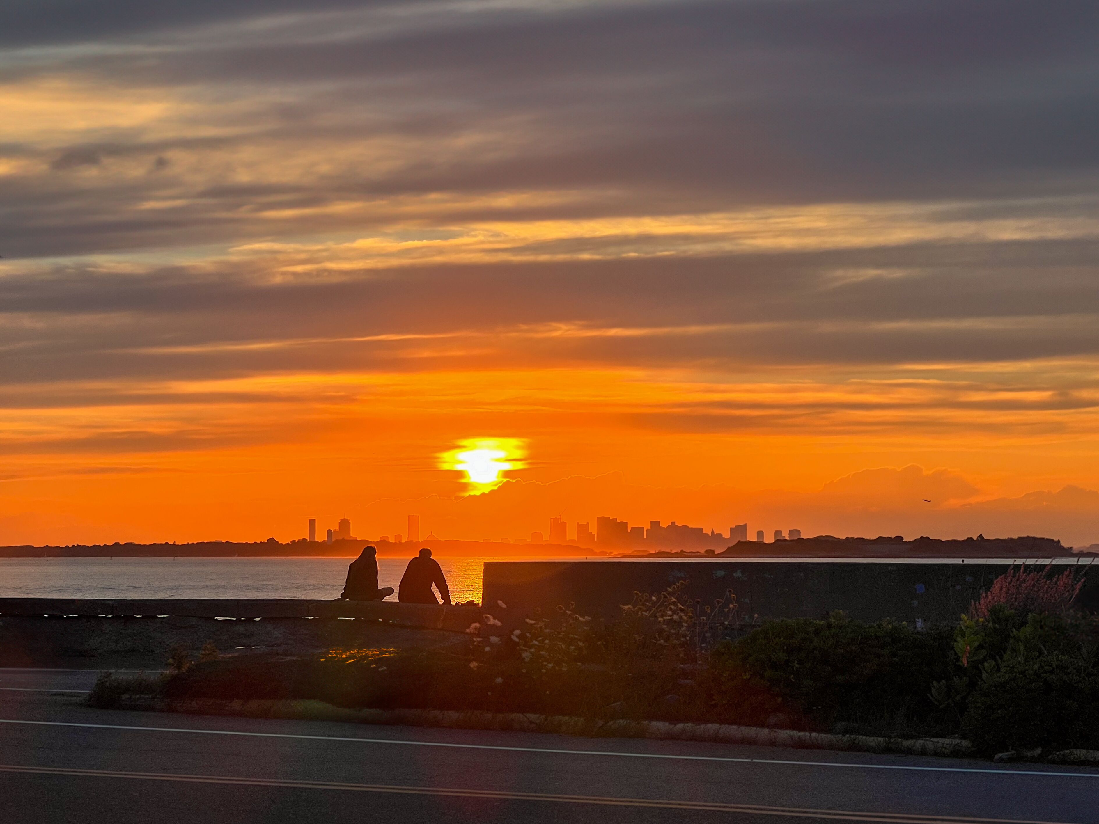sunset over the city with a silhouette of a man and woman sitting on a stone wall