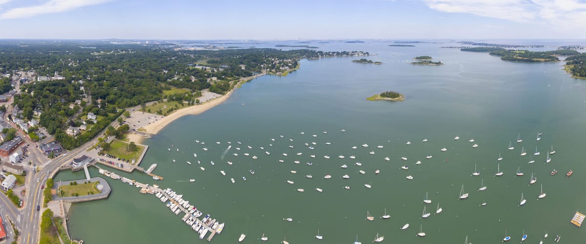 A coastal town with a marina filled with boats, surrounded by greenery and small islands.