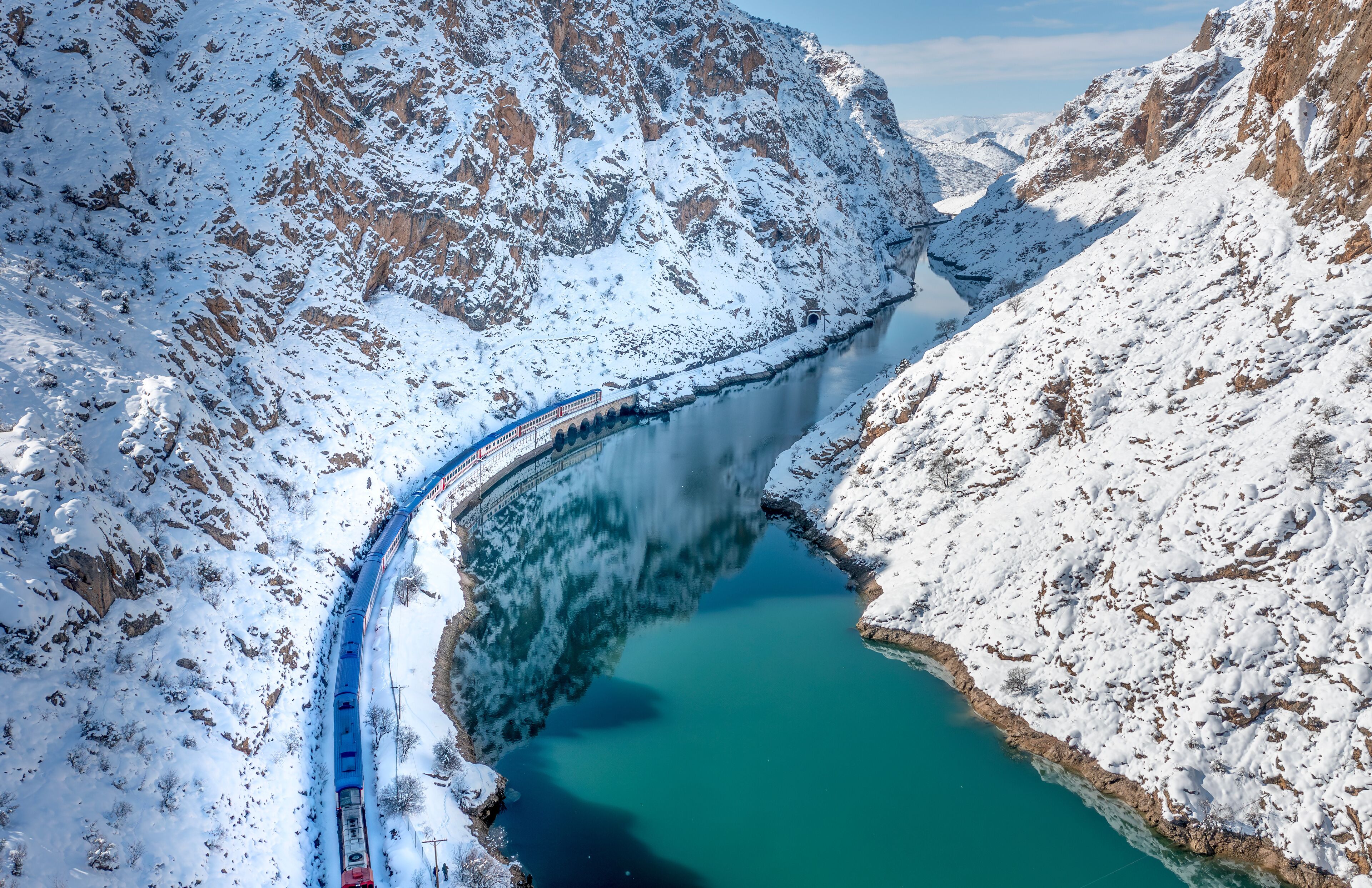 A snow-covered mountain landscape with a turquoise lake and a train track.