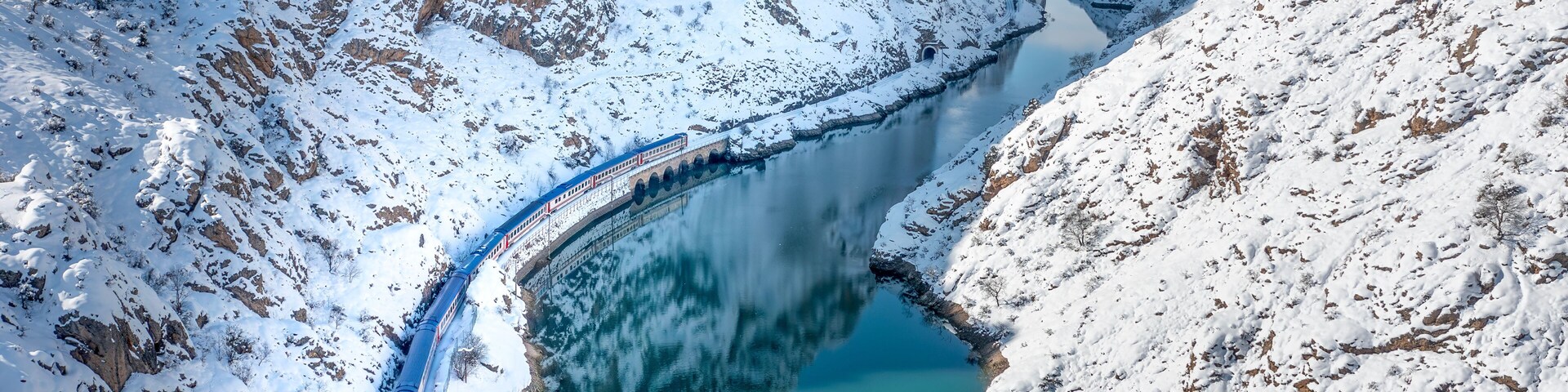 A snow-covered mountain landscape with a turquoise lake and a train track.