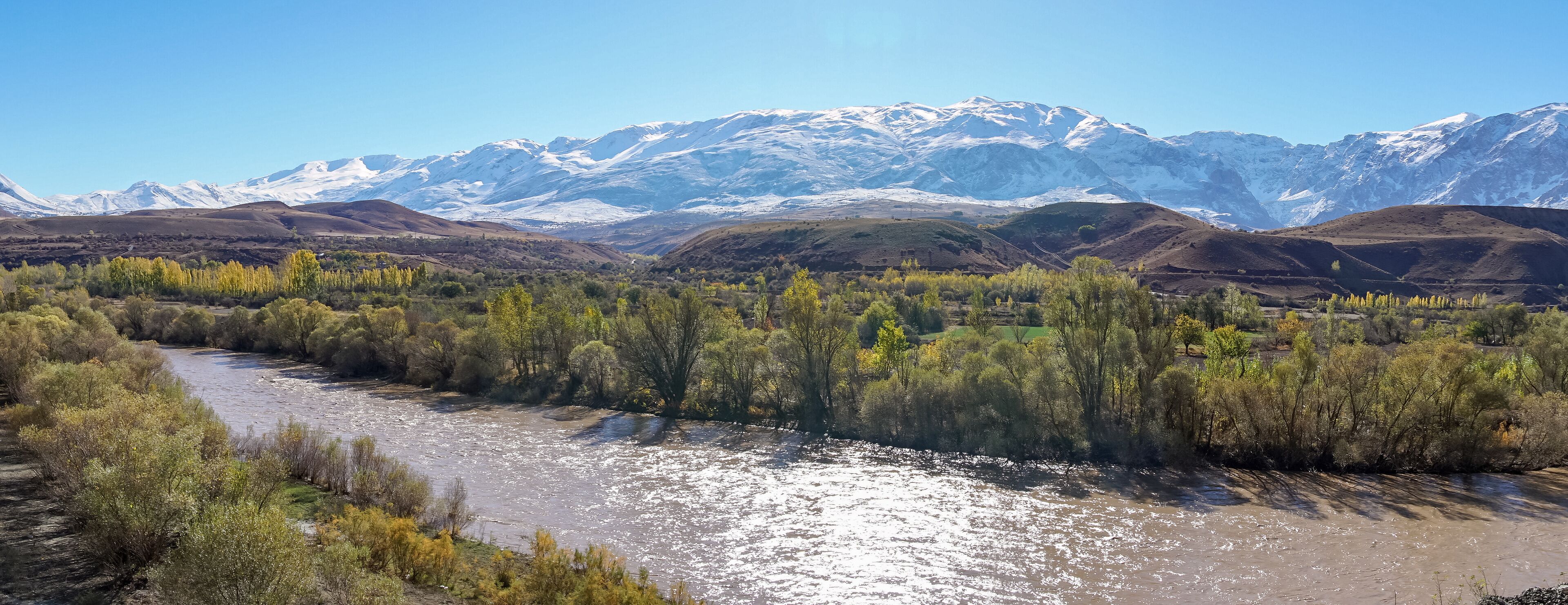 A river flowing through a valley with snow-capped mountains in the background.